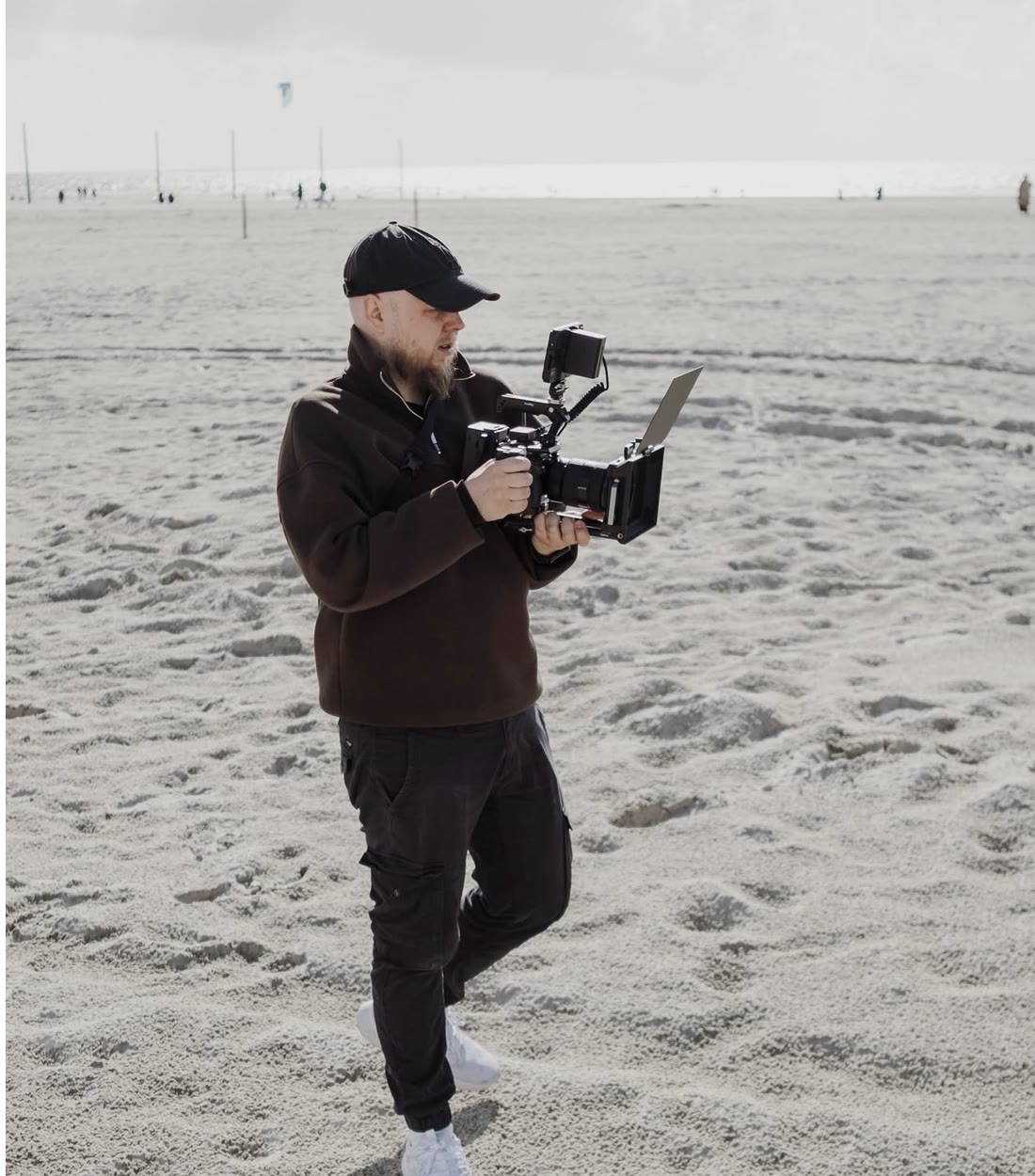 Leon Saß mit Cap und Kamera-Rig läuft über einen weiten Sandstrand und schaut auf den Monitor